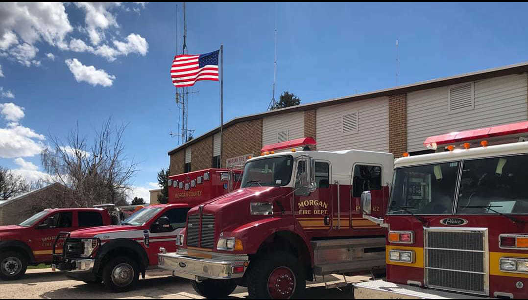 Fire station with red fire trucks parked outside, American flag waving.