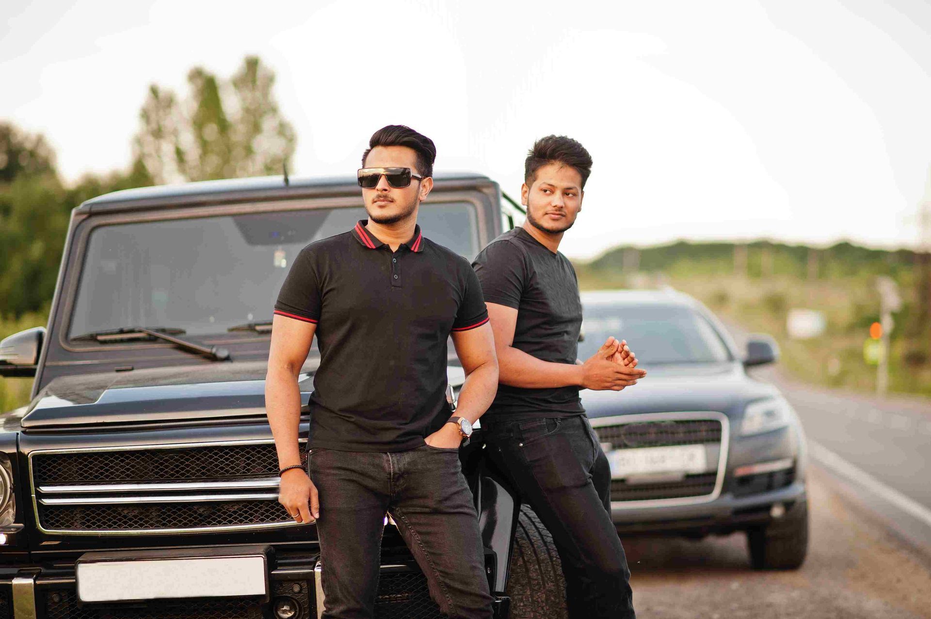 Two men are standing next to a car on the side of the road.