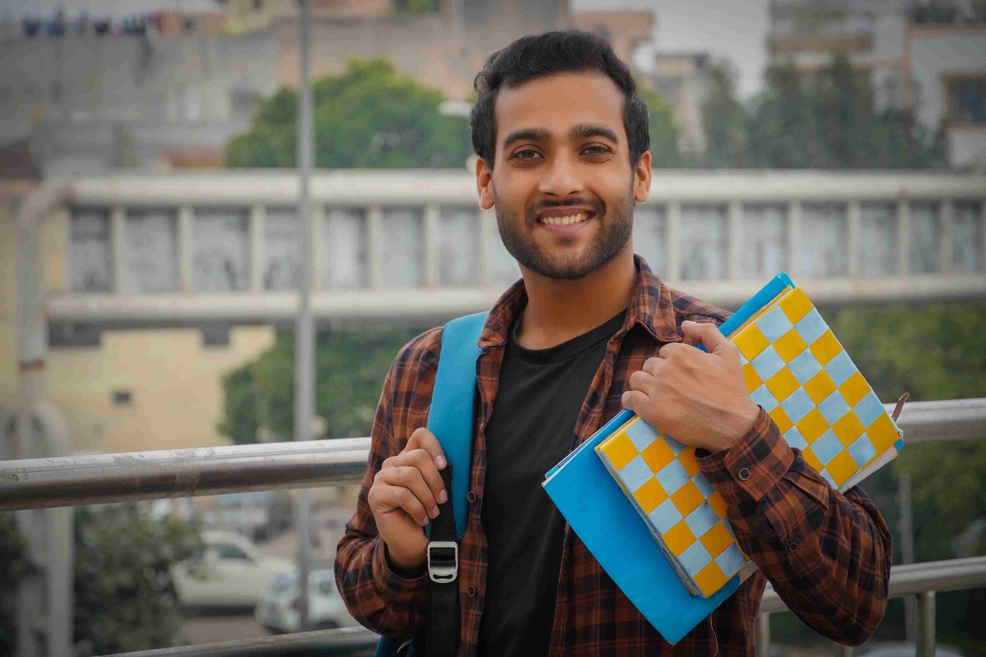 A young man with a backpack is holding a book and smiling.