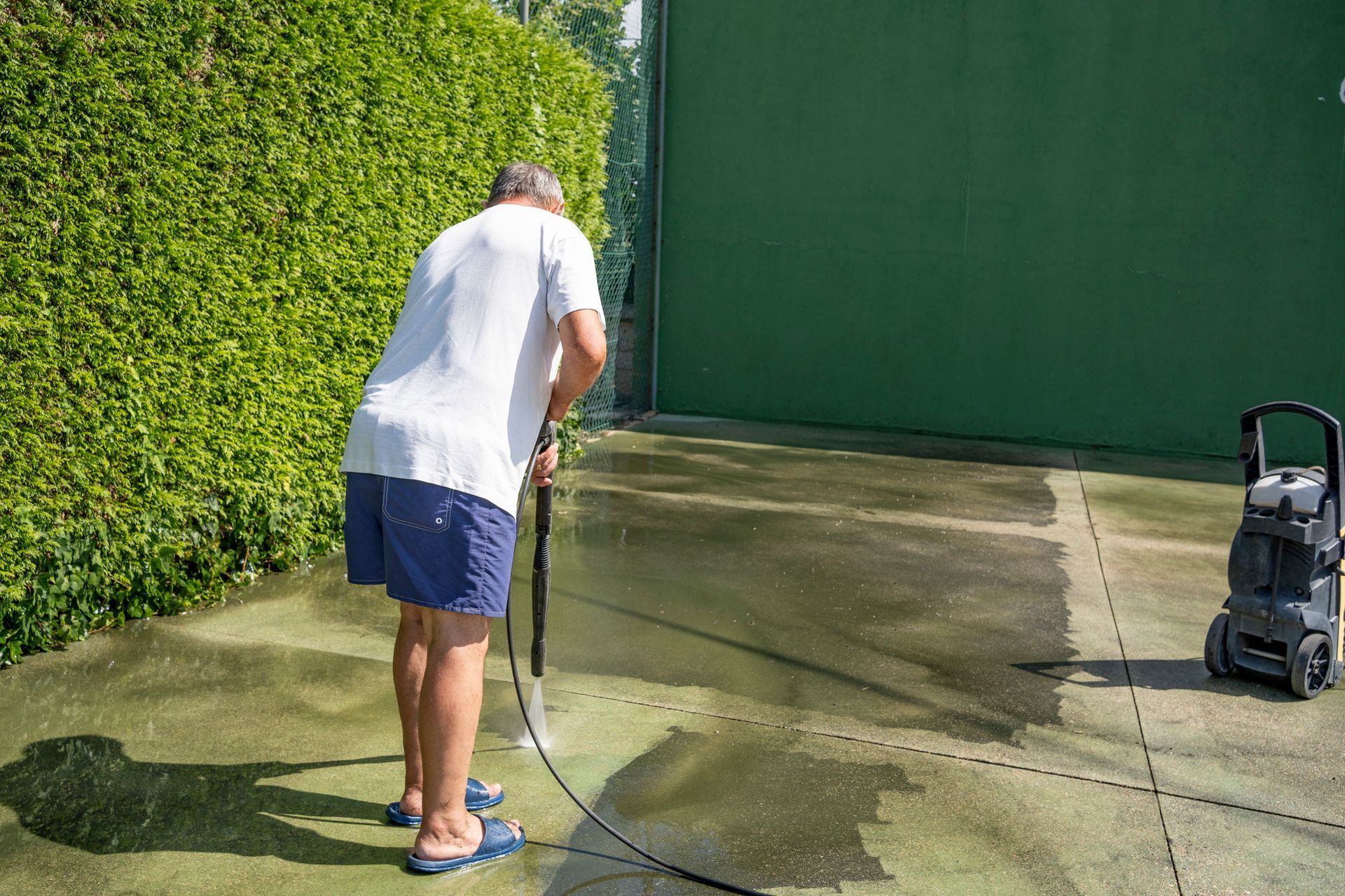 Senior man washes the floor of a tennis court.