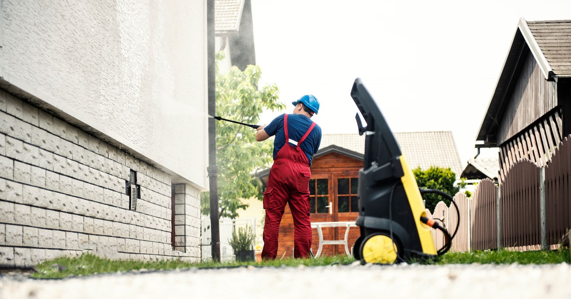 A worker is pressure washing a wall of a house.