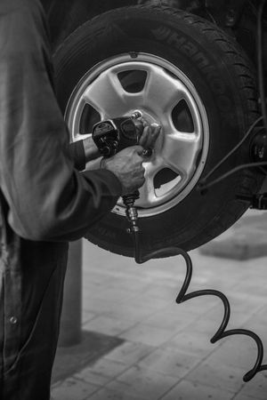 A mechanic uses a pneumatic impact wrench to tighten the lug nuts on a car tire in an auto repair shop.