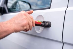A person unlocking a white car door with a key featuring a red and yellow plastic cover.