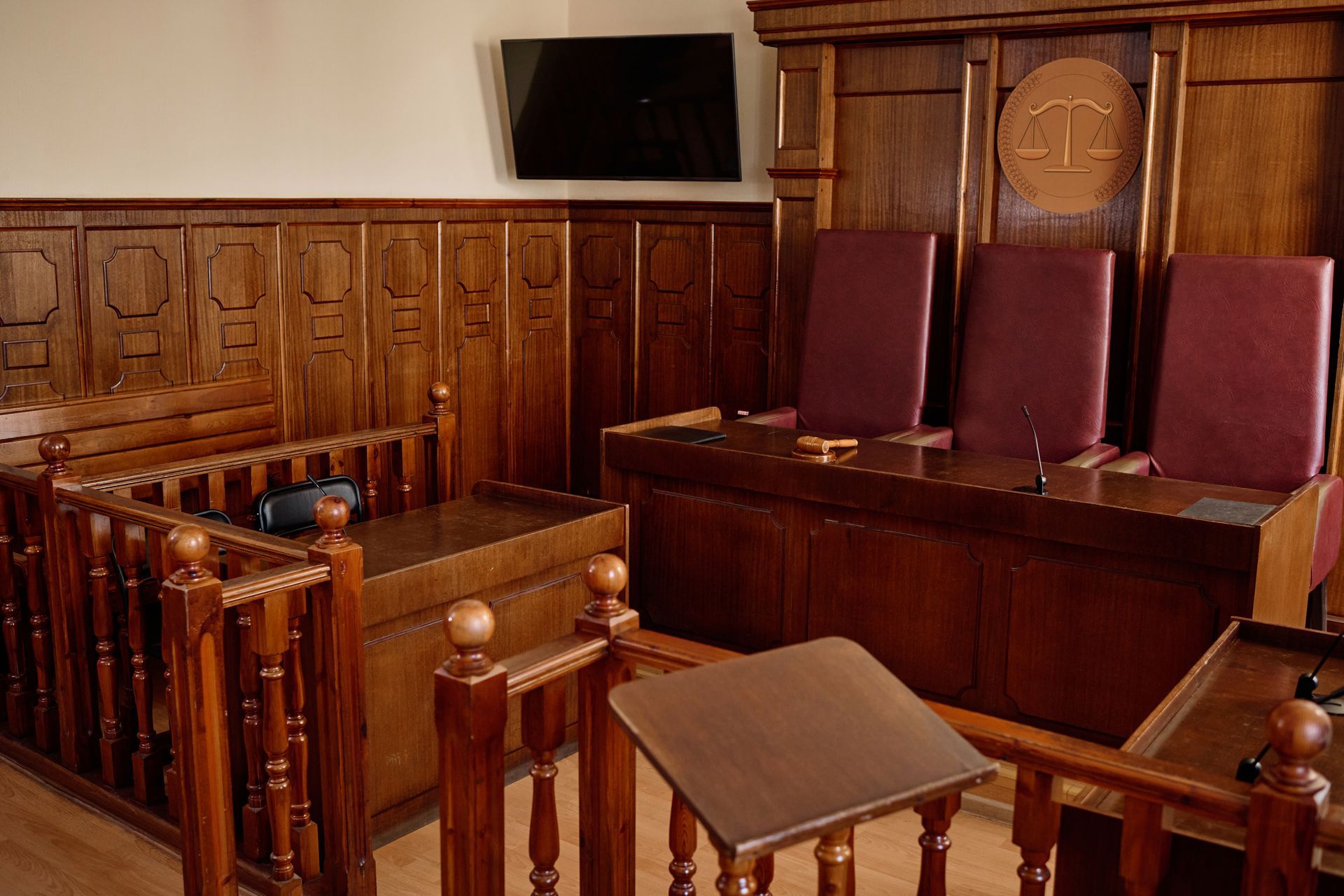 A courtroom with a wooden bench and chairs and a television on the wall.