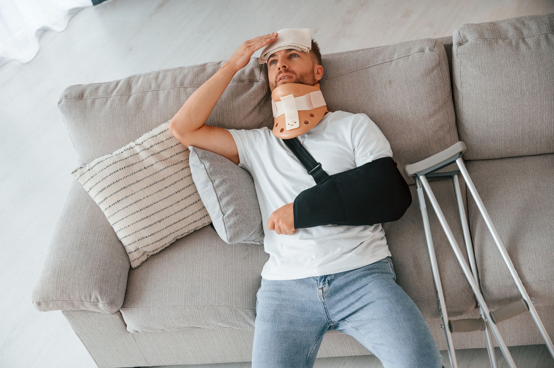 A man with a neck brace is laying on a couch with crutches.