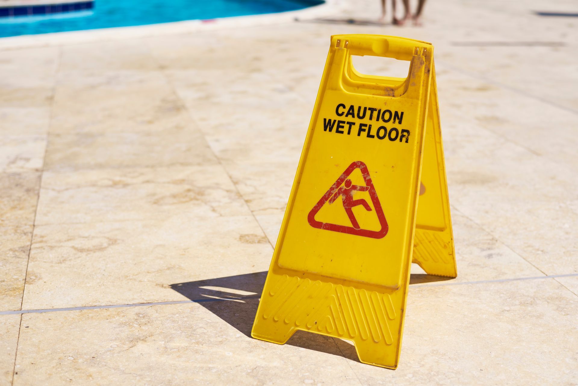 A yellow caution wet floor sign is sitting on a tiled floor next to a pool.