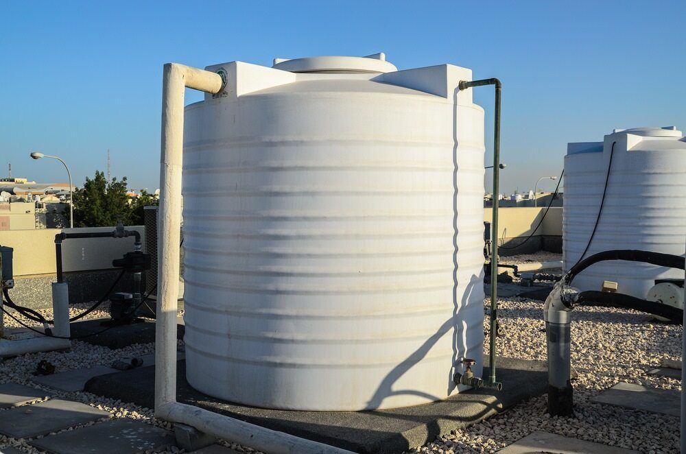 A Large White Water Tank is Sitting on Top of a Gravel Covered Roof — Tink's Water Tank Cleaning in Harrington, NSW