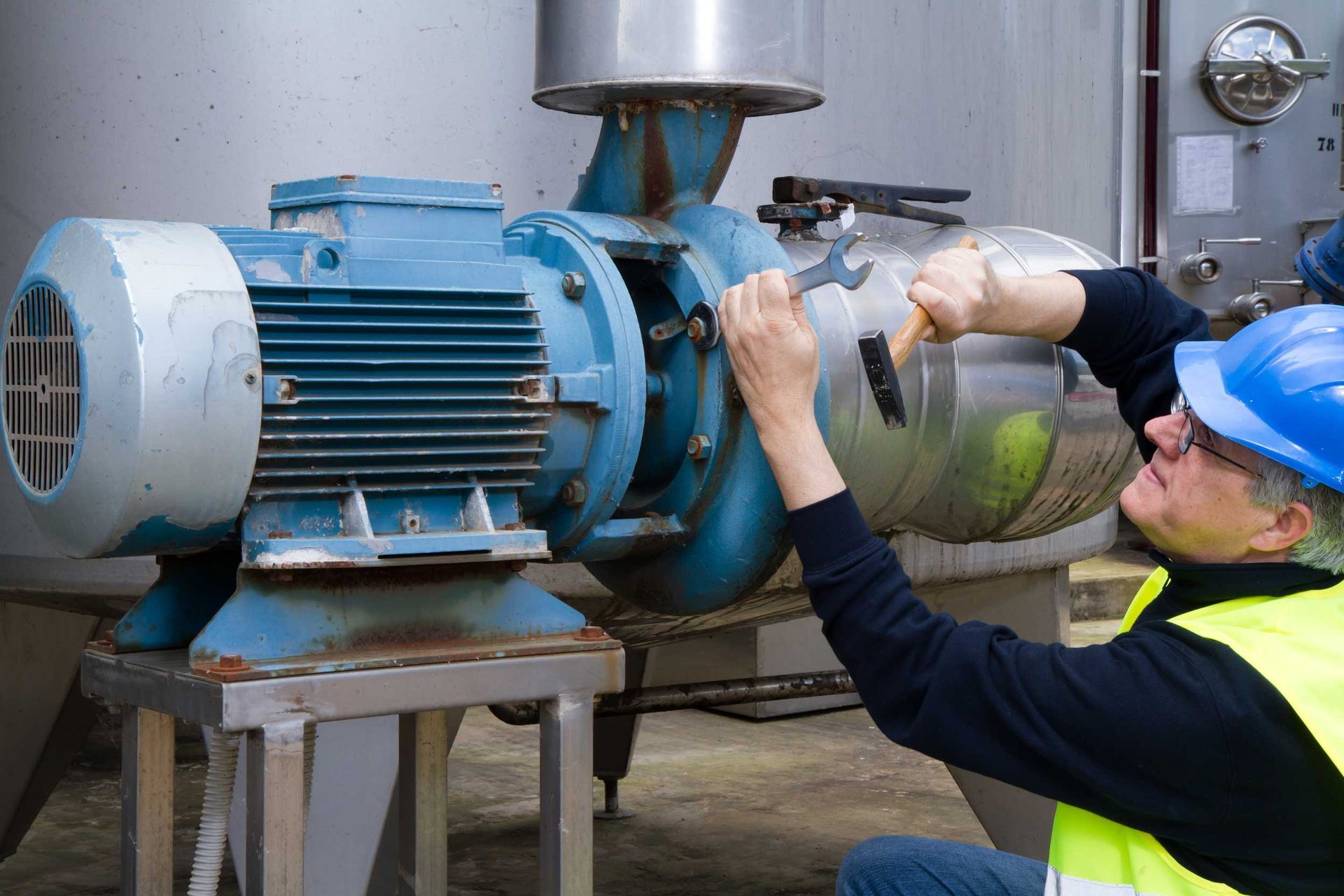 A worker performing maintenance on industrial machinery using a wrench.