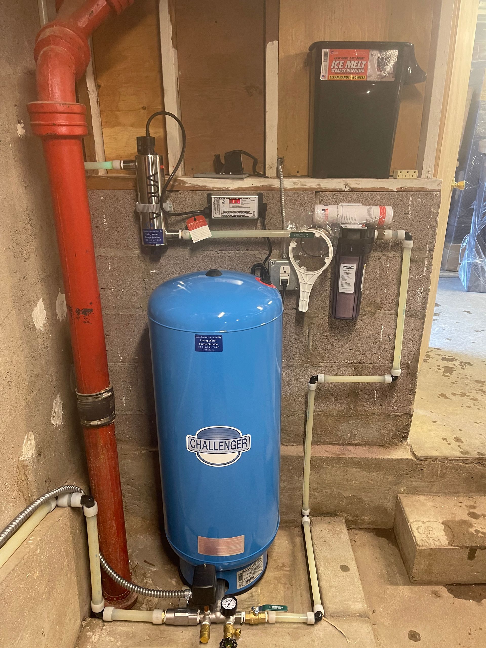Blue well water tank, piping, filters, and pump installed in a basement setting.