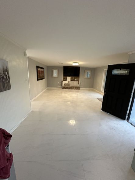 Empty room with white floor and walls, fireplace with a TV. Black door.