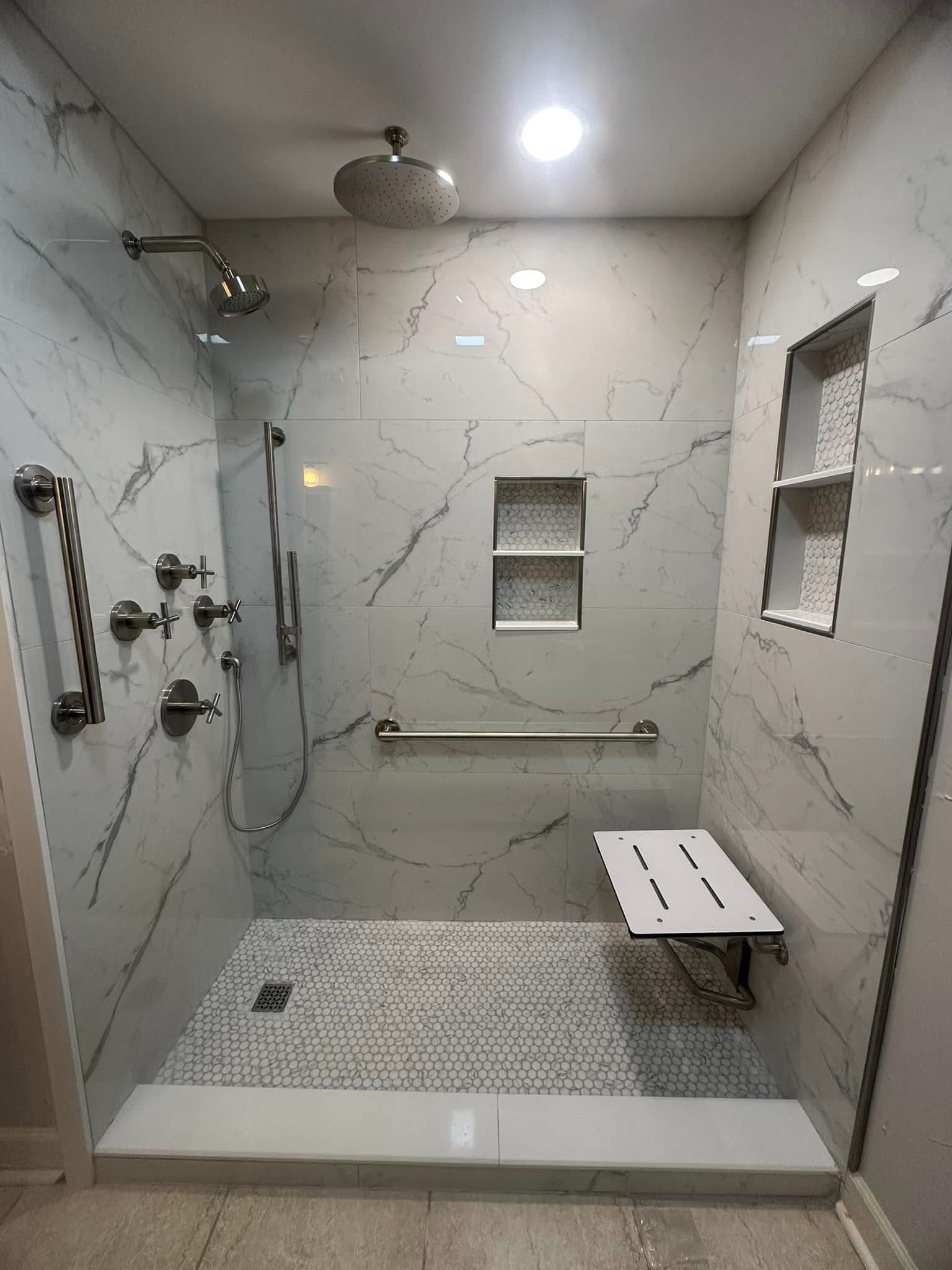 Accessible shower with marble-look tile, grab bars, built-in niches, and a fold-down seat.