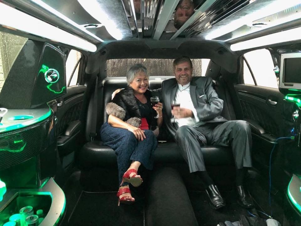 A man and a woman are sitting in the back seat of a limousine.