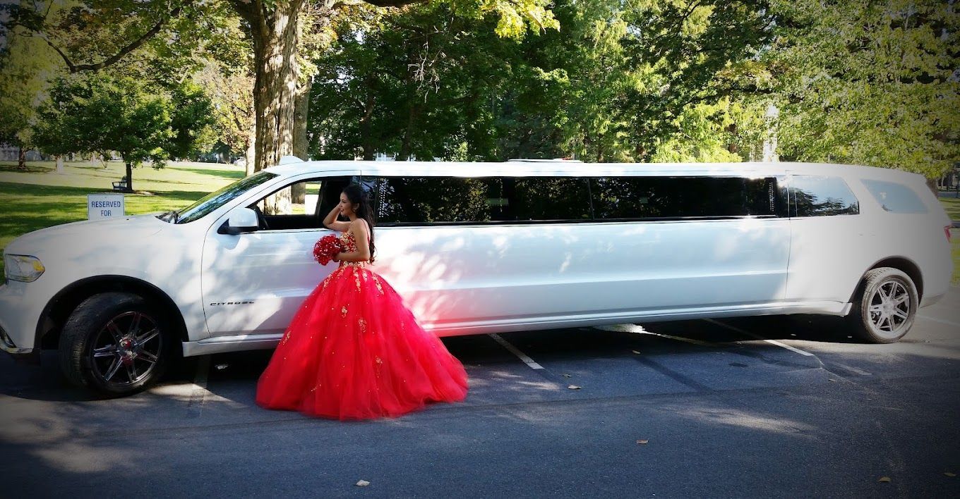 A woman in a red dress is standing next to a white limousine.