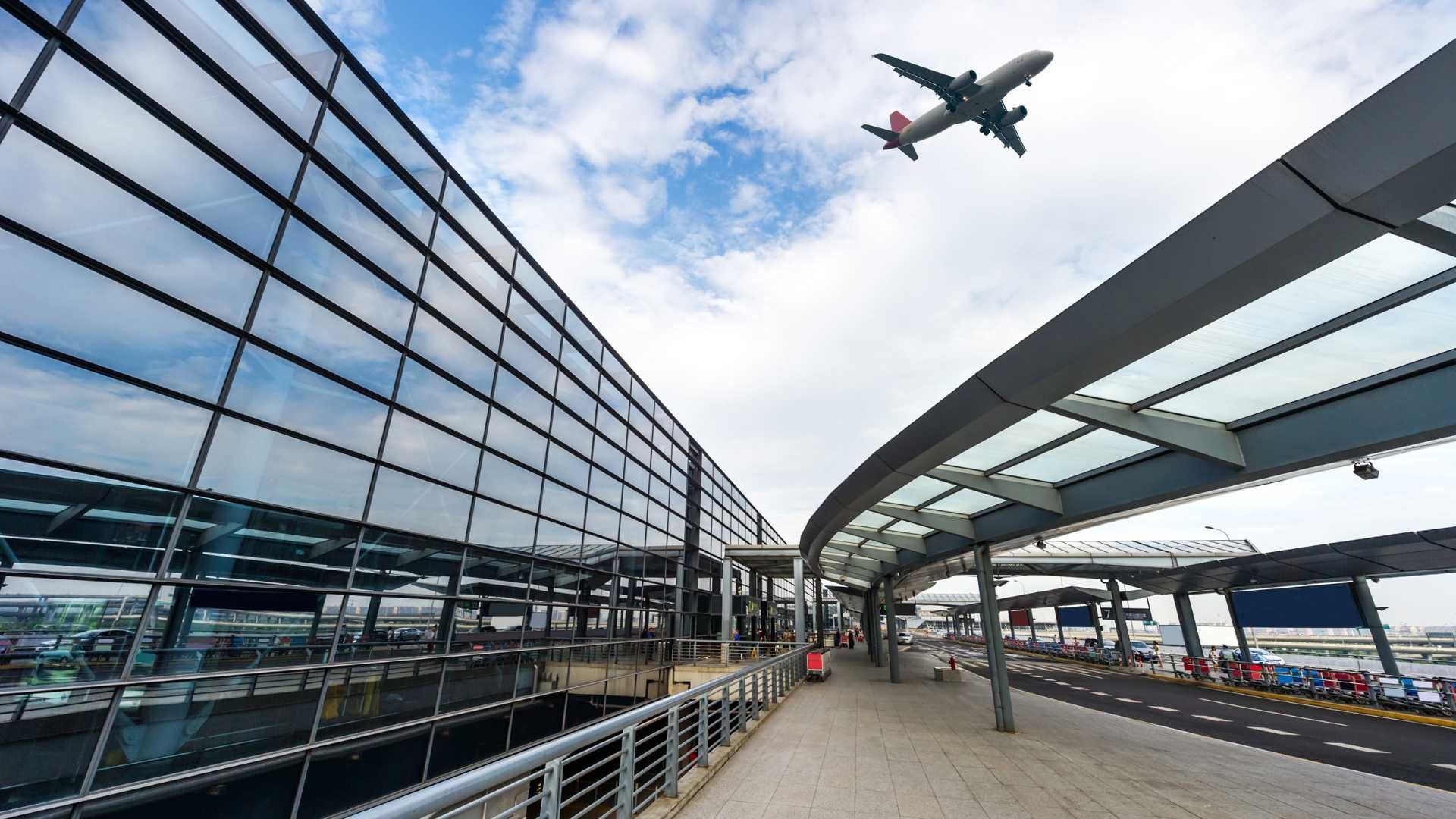 An airplane is flying over an airport terminal.