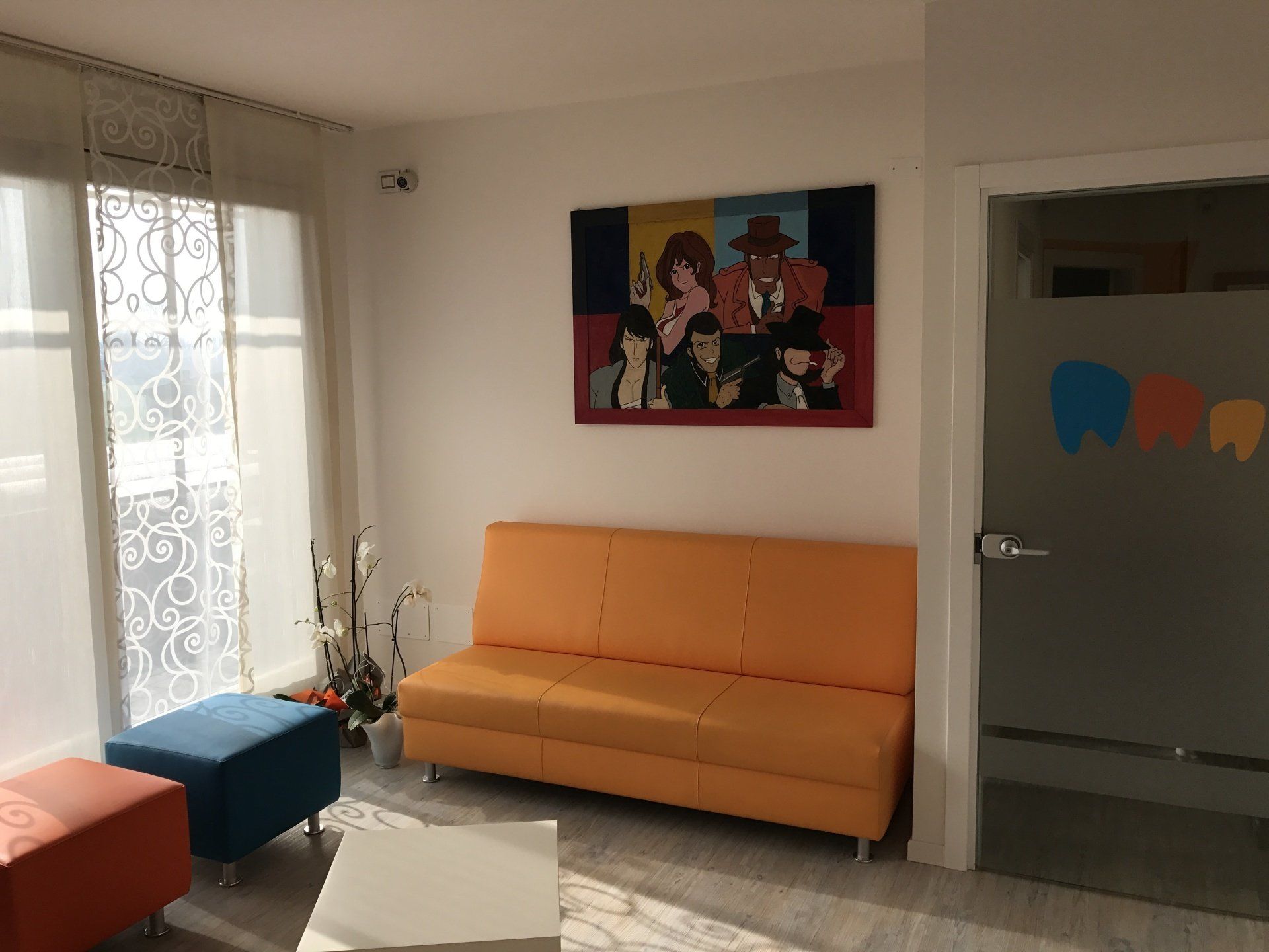 Sala d'attesa con divano arancione, disegni di cartoni animati e porta smerigliata con disegno di denti.