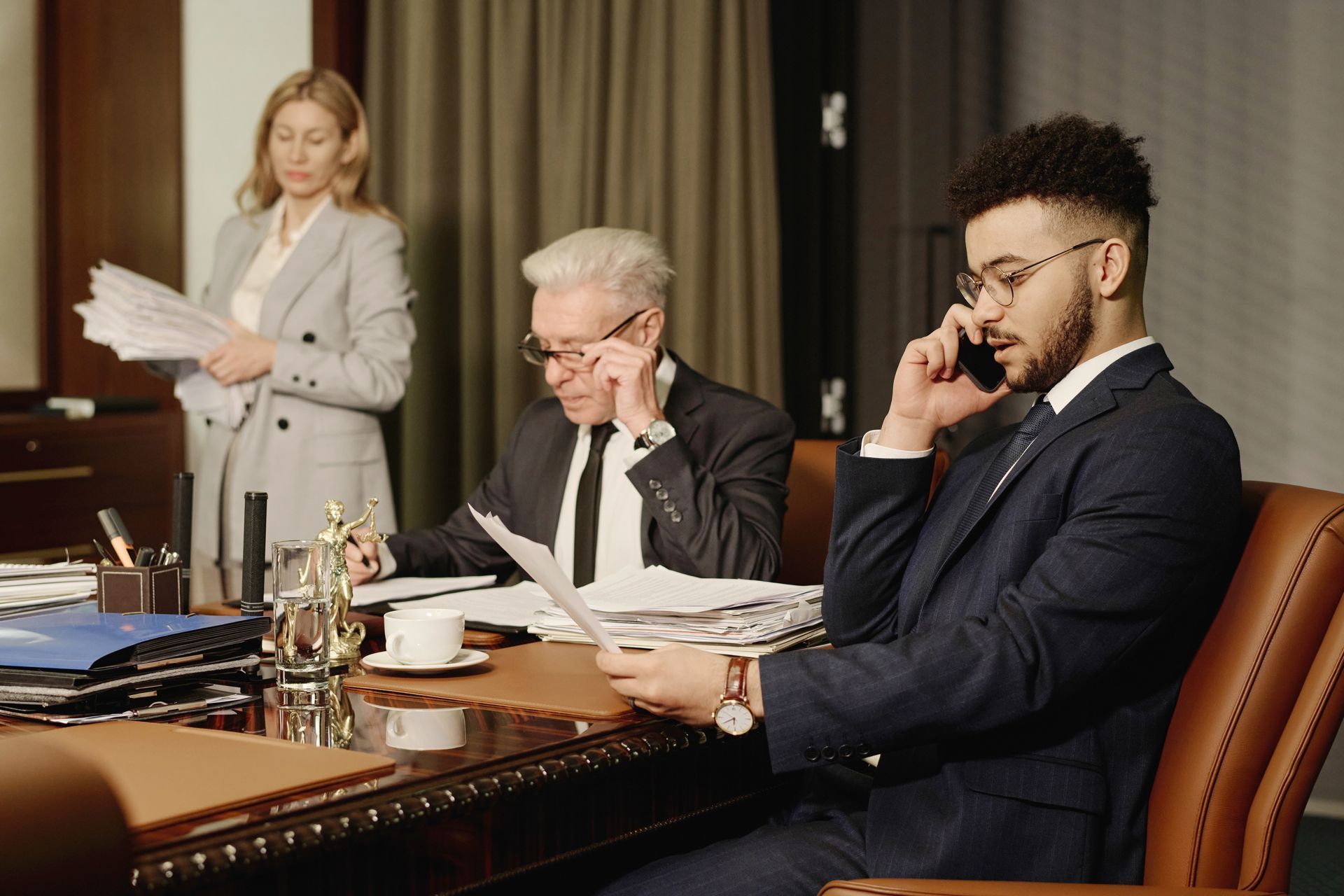 A man in a suit is sitting at a desk talking on a cell phone.