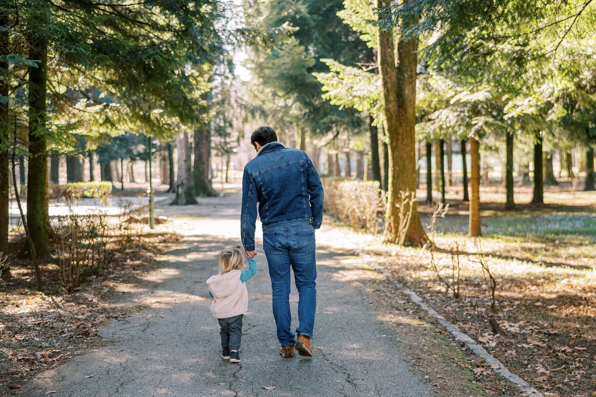 A man and a little girl are walking down a path in the woods.