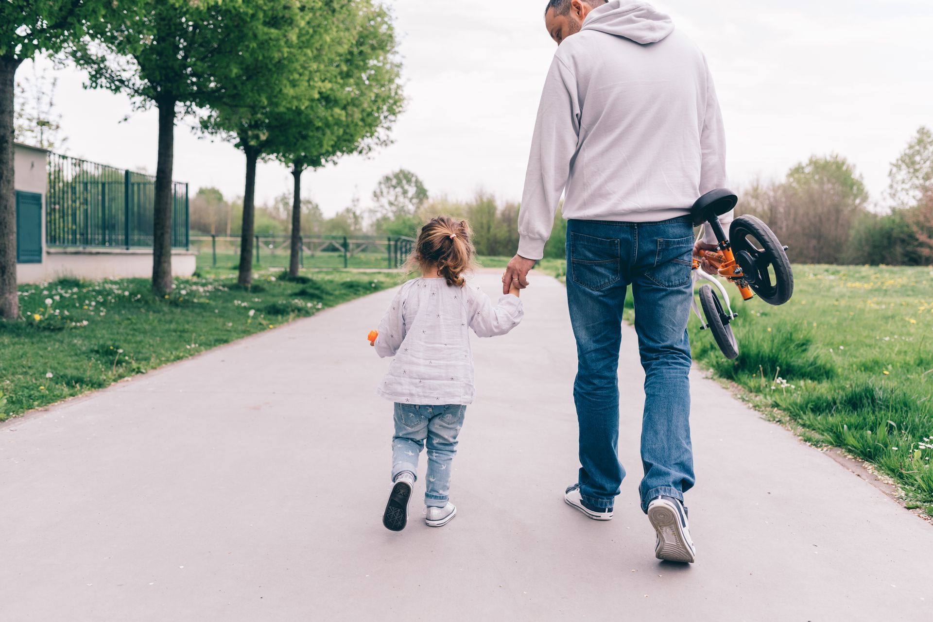 A man and a little girl are walking down a path holding hands.