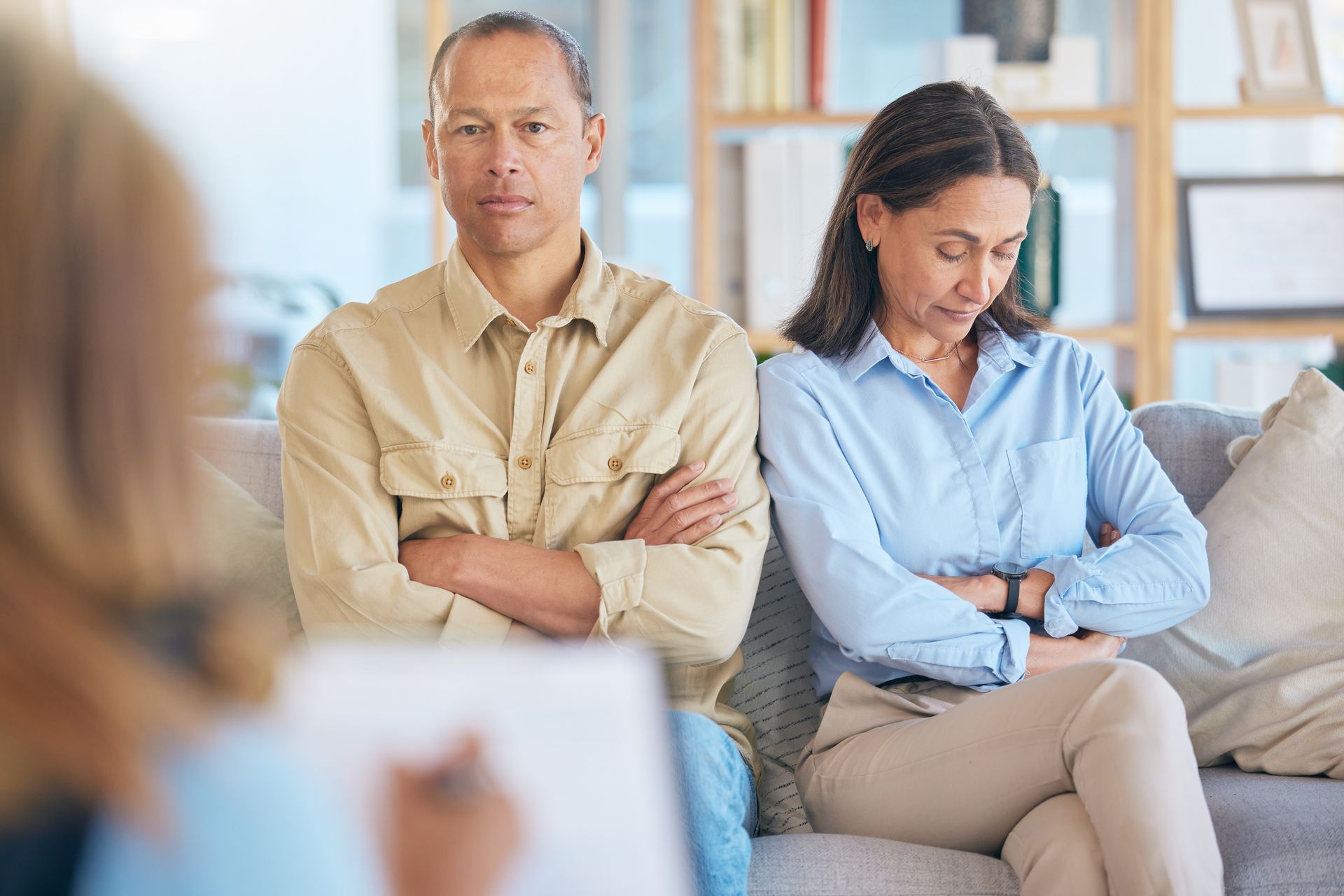 A man and a woman are sitting on a couch with their arms crossed.