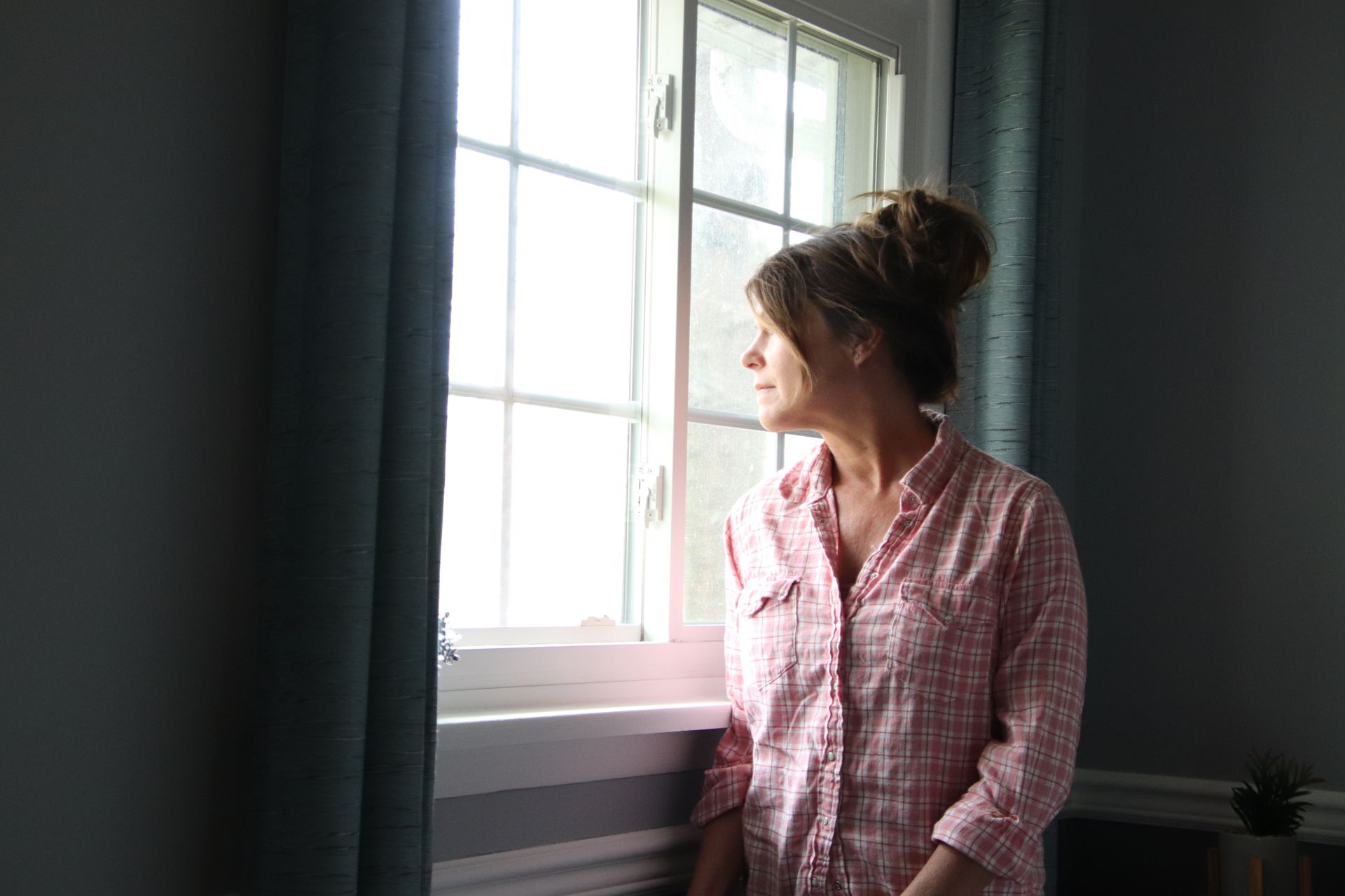 A woman in a pink shirt is looking out of a window.