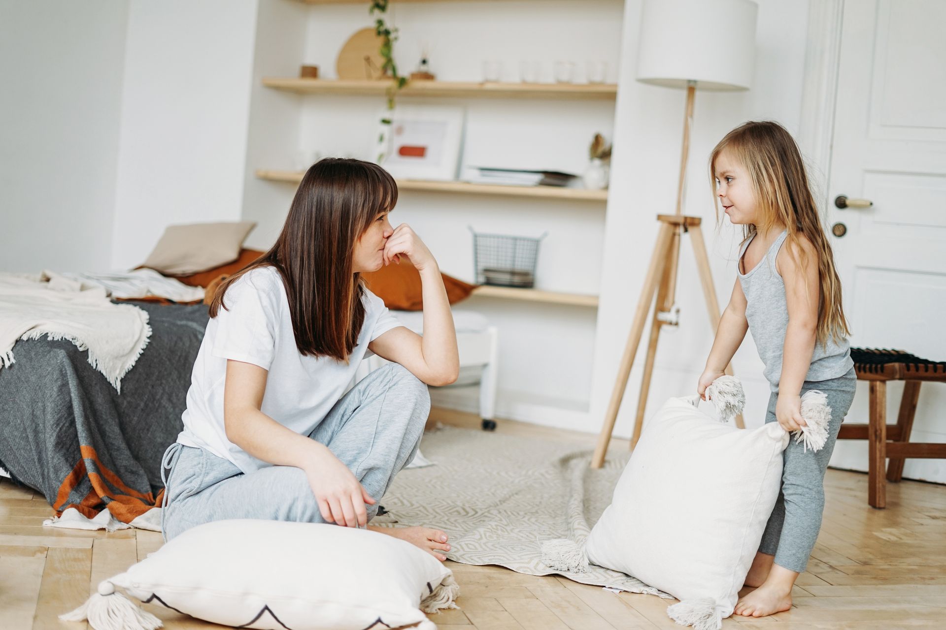 A woman and a little girl are playing with pillows in a living room.