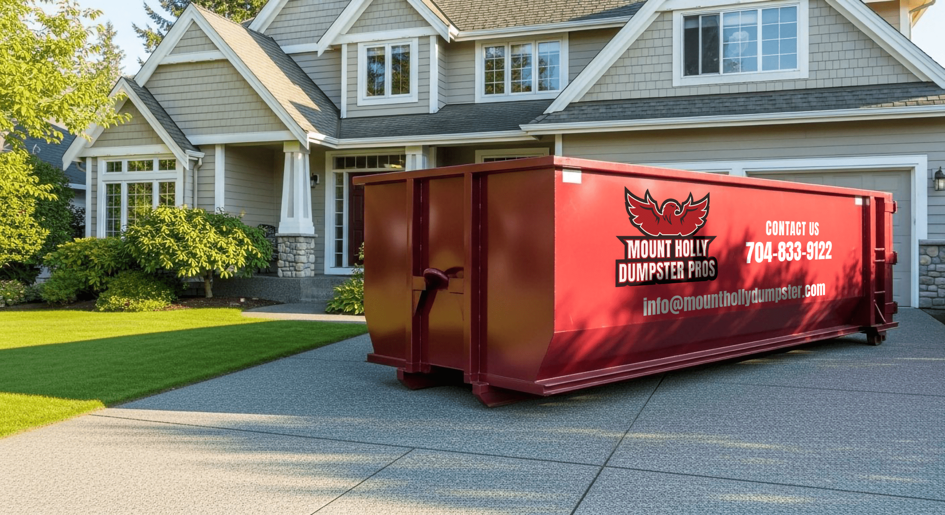 Maroon dumpster on a paved driveway in front of a gray house with a green lawn.