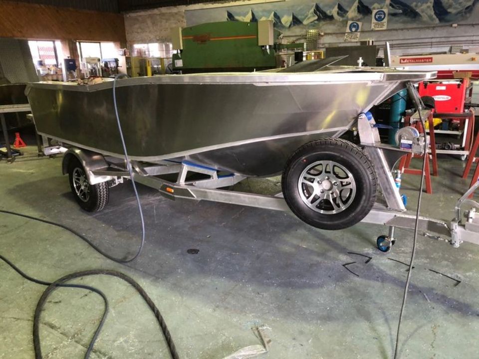 A stainless steel boat is on a trailer in a garage.