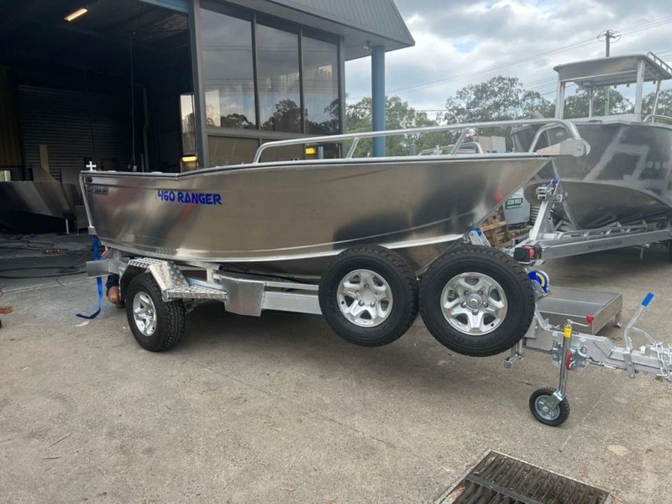 A silver boat is on a trailer in front of a building.
