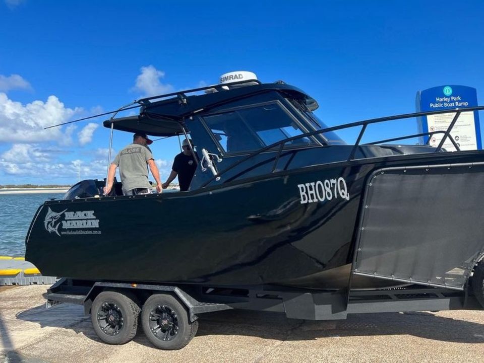 A man is standing next to a black boat on a trailer.