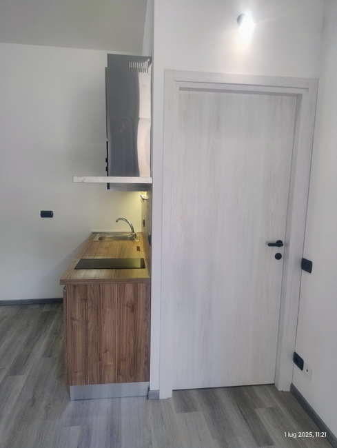 Una mano che mescola un cappuccino schiumoso in una tazza nera Mado, un croissant e dei bicchieri d'acqua su un tavolo.