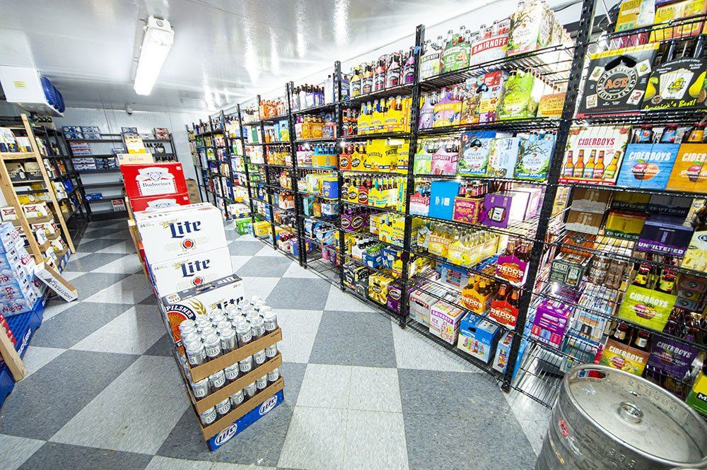 A liquor store interior with stocked shelves of beverages, Miller Lite display, and a keg on the floor.