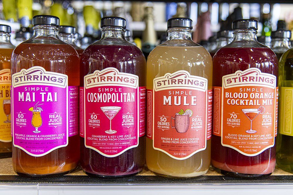 Bottles of Stirrings cocktail mixers on a shelf, flavors include Mai Tai, Cosmopolitan, Mule, and Blood Orange.