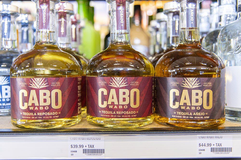 Three bottles of Cabo Wabo tequila with red and gold labels on a store shelf.