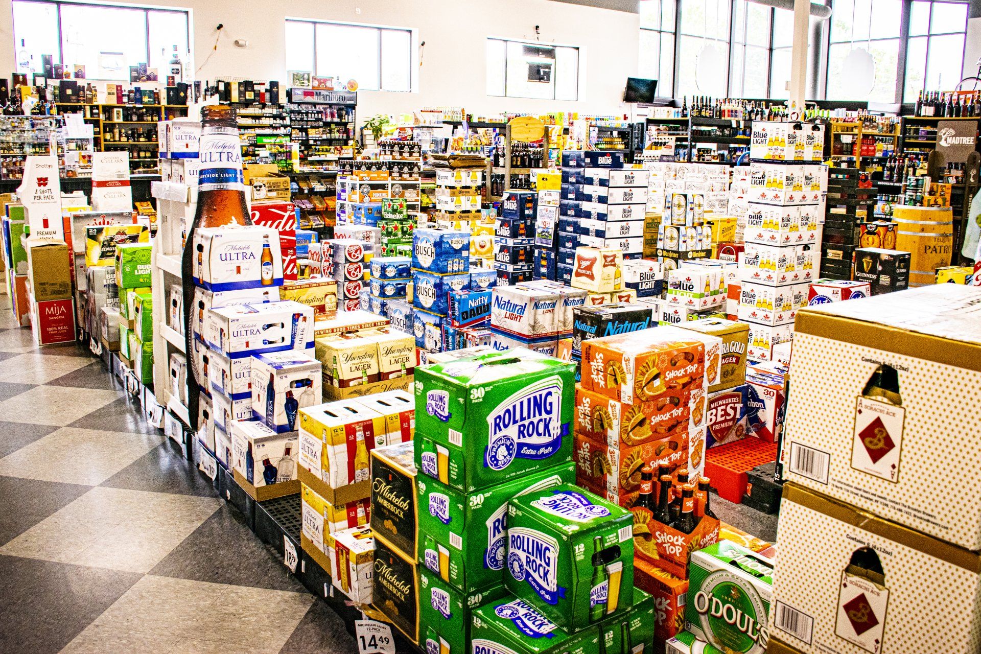 Liquor store aisle filled with stacked boxes of beverages, including beer and soda.