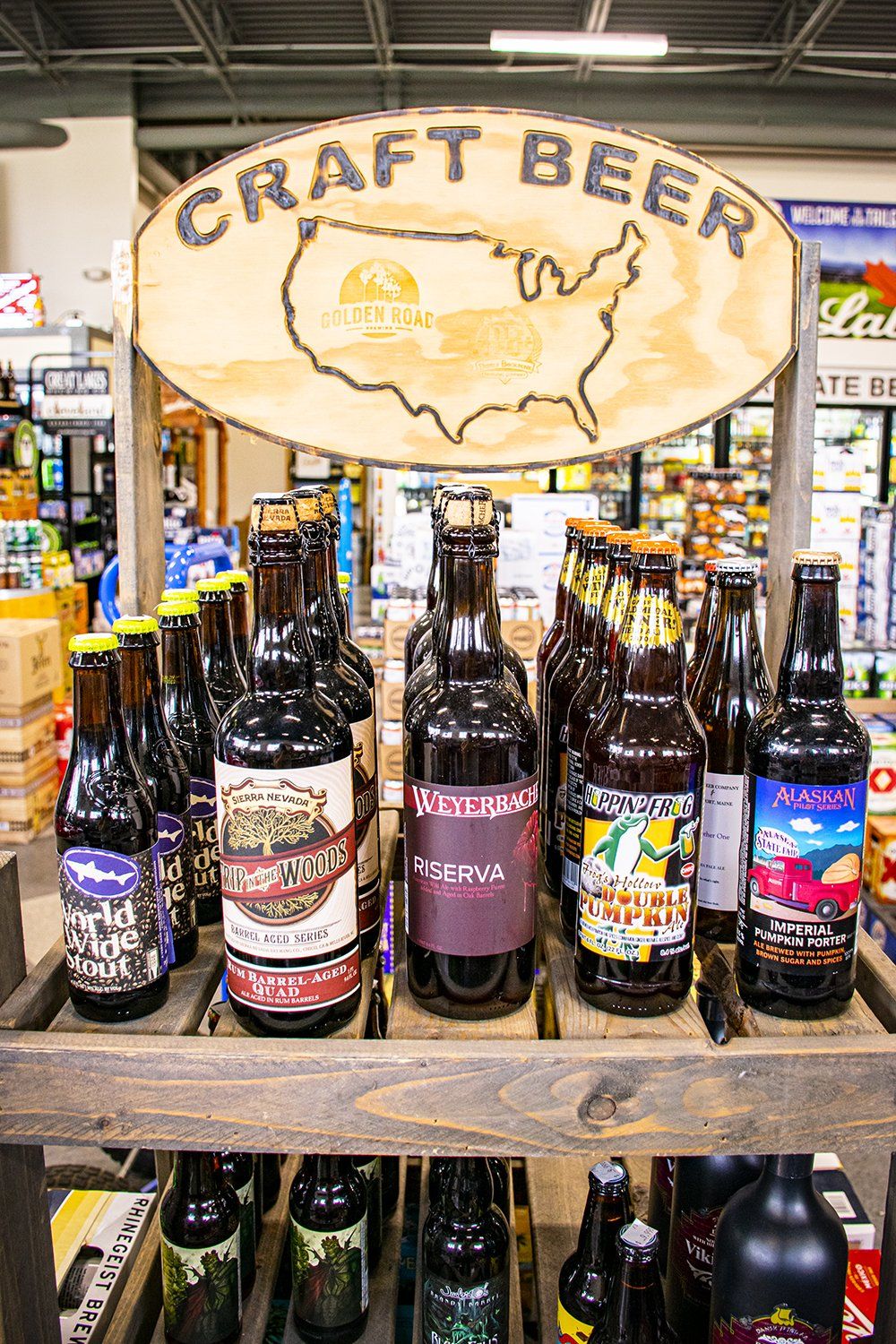 Craft beer display with bottles on wooden shelves under a sign shaped like the US, indoors.