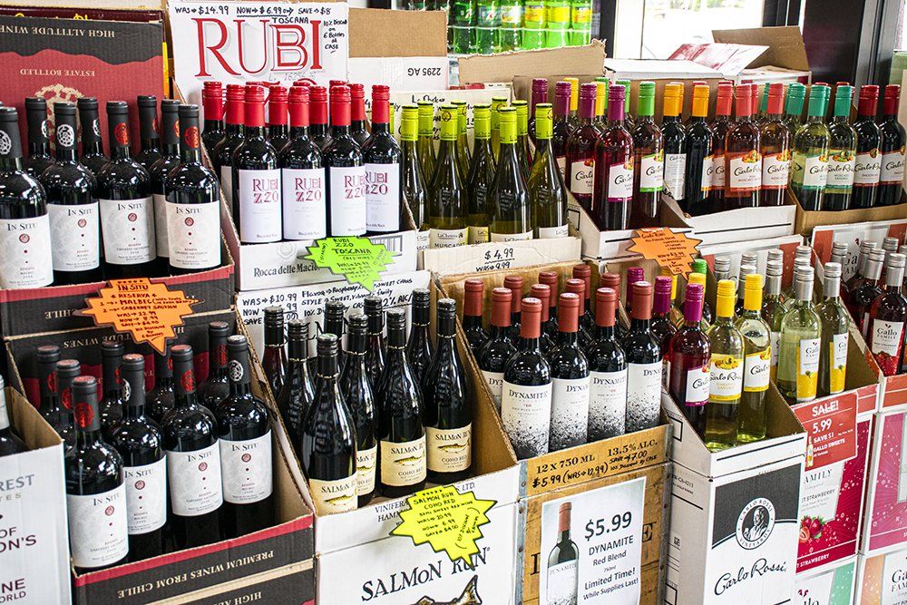 Wine bottles displayed in boxes at a store; red, white, and green bottles are visible.