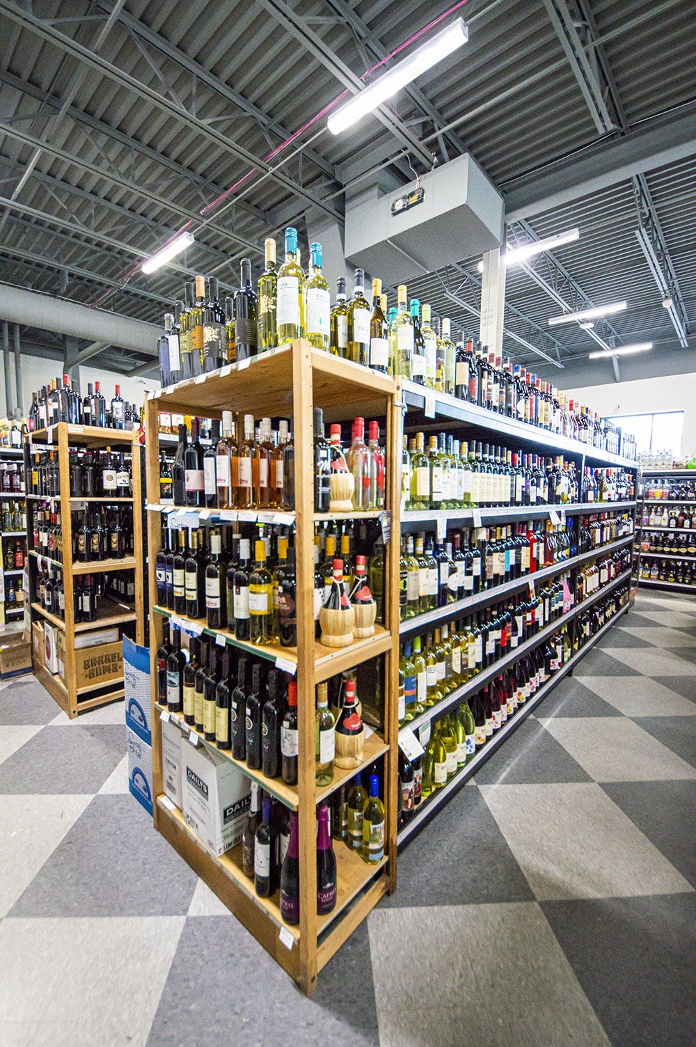 Wine bottles on shelves in a brightly lit store. Rows of various bottles, wooden shelves, and checkered floor.