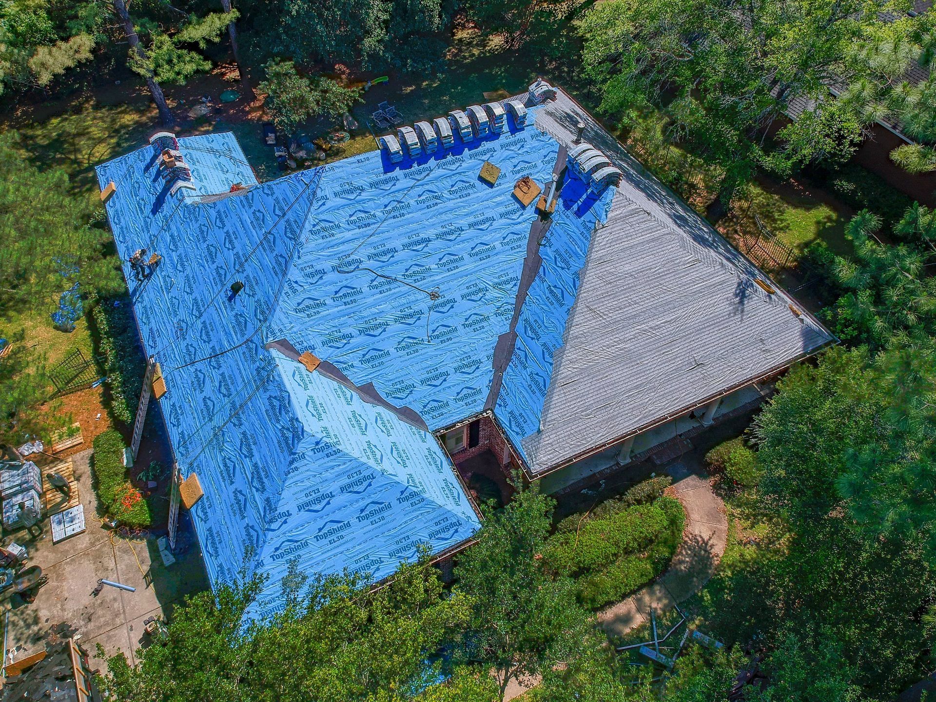 An aerial view of a house with a blue tarp on the roof.