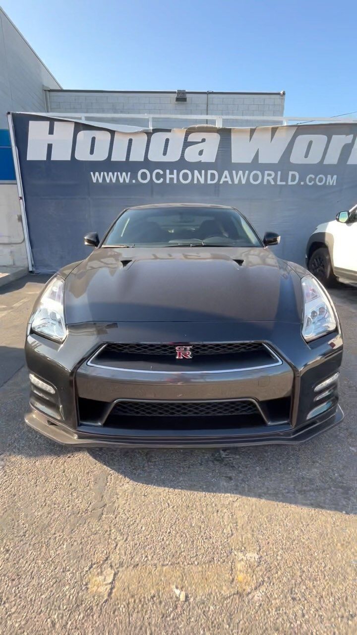 A black nissan gtr is parked in front of a honda world sign.