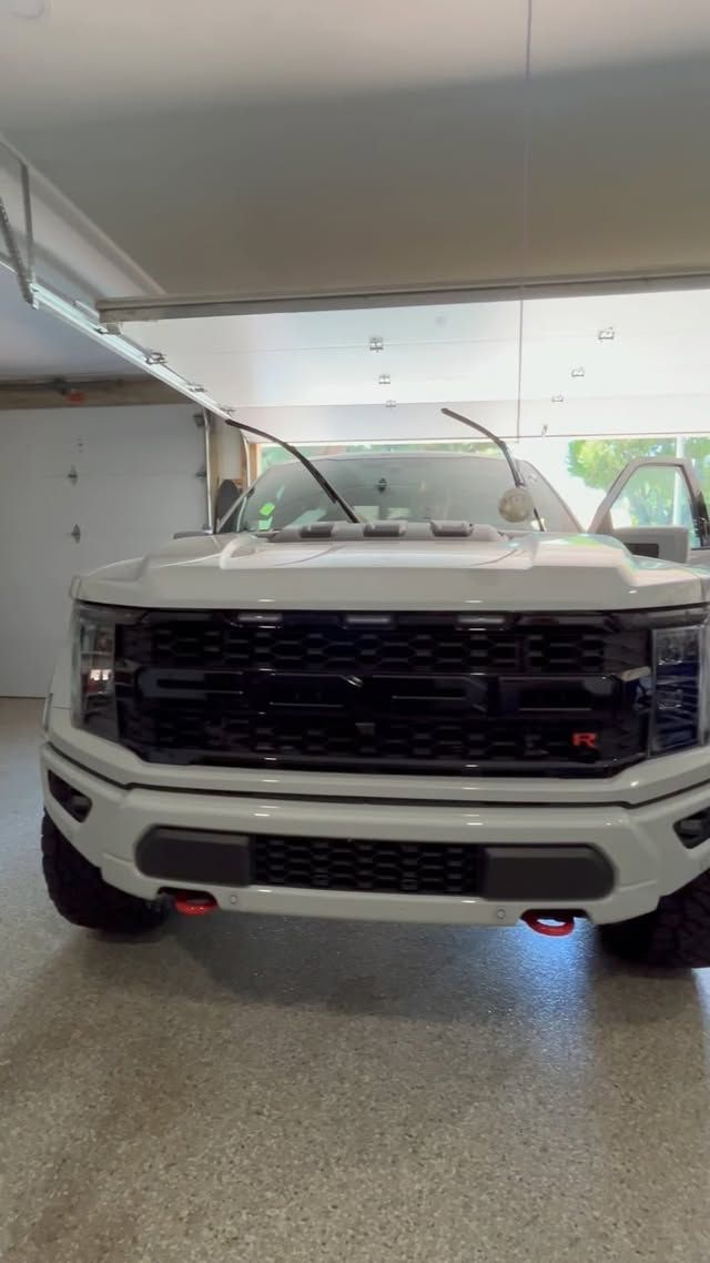 A white ford raptor is parked in a garage.