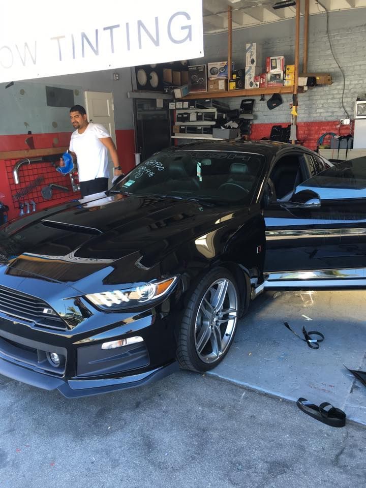 A man is standing next to a black car under a sign that says low tinting