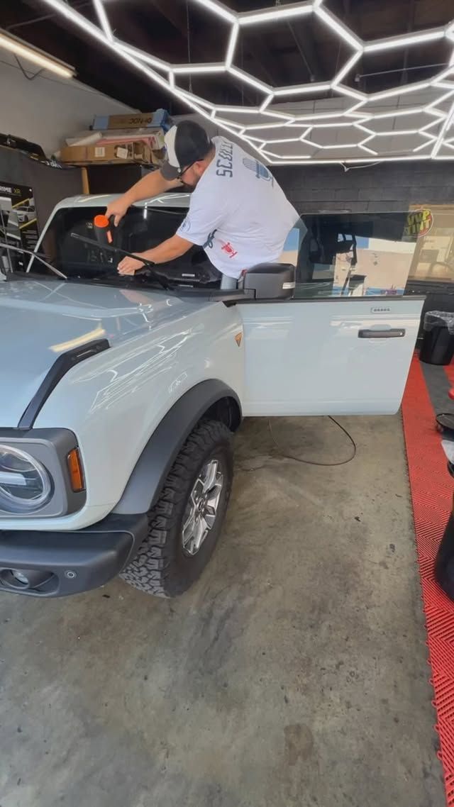 A man is cleaning the windshield of a white truck in a garage.