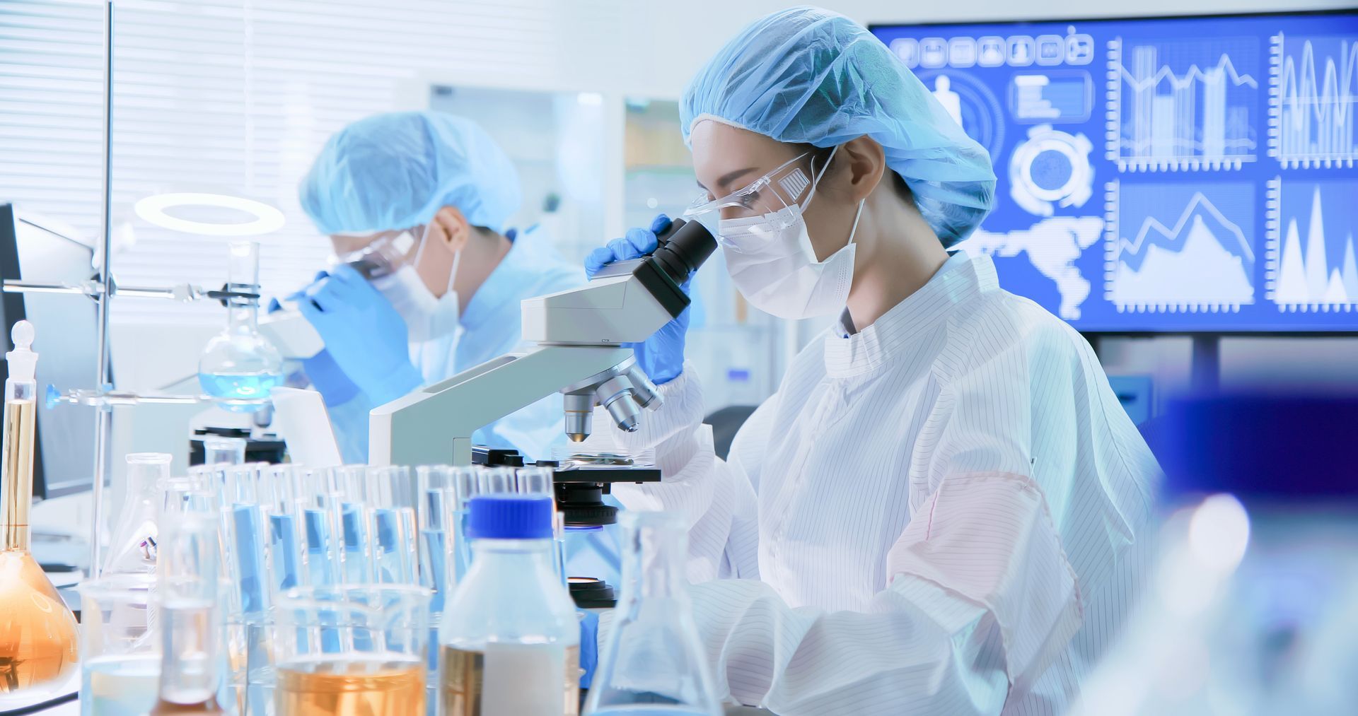 Scientists in white lab coats and blue caps working with lab equipment in a research laboratory