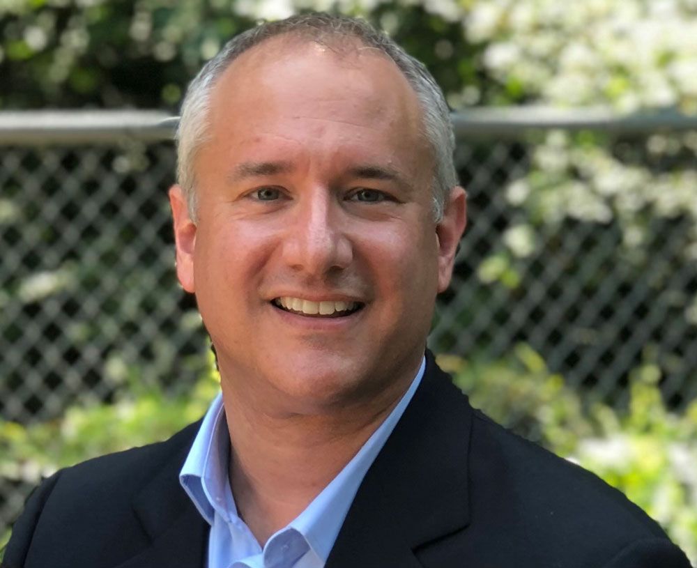 DR. CHRISTOPHER DEITZ in a suit and blue shirt is smiling for the camera.