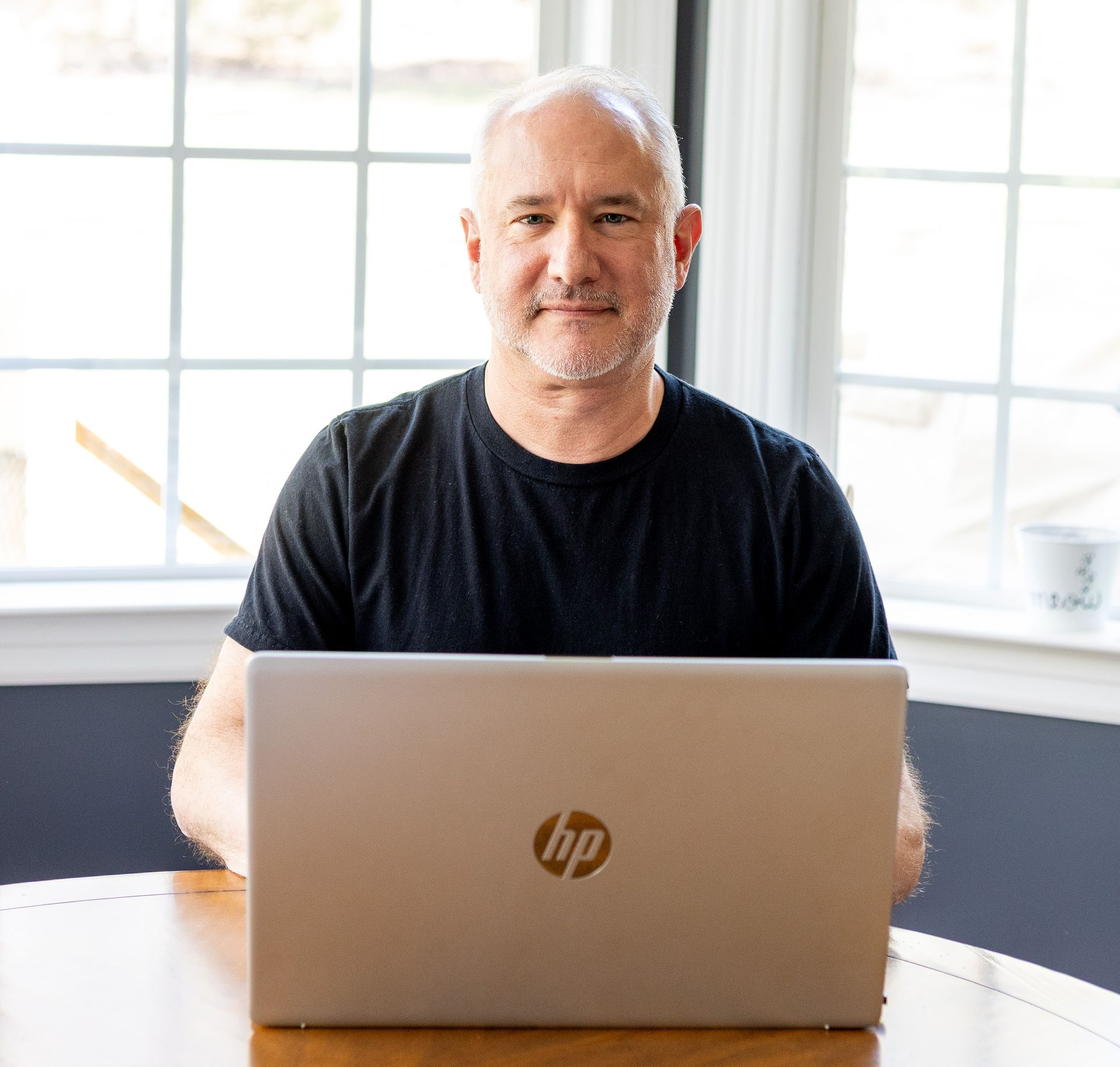 Man in a blue shirt and black jacket smiles in an outdoor setting.