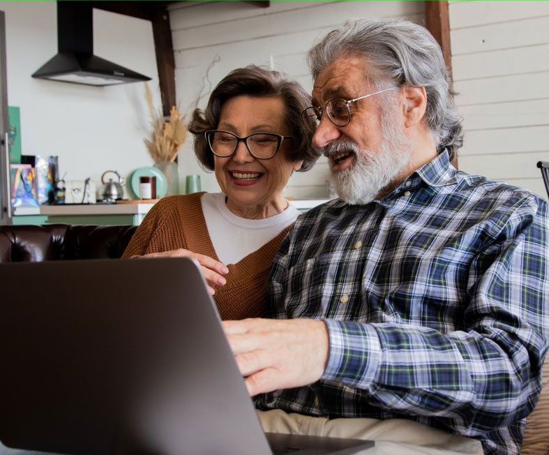 An older couple smiling while looking at a laptop computer.