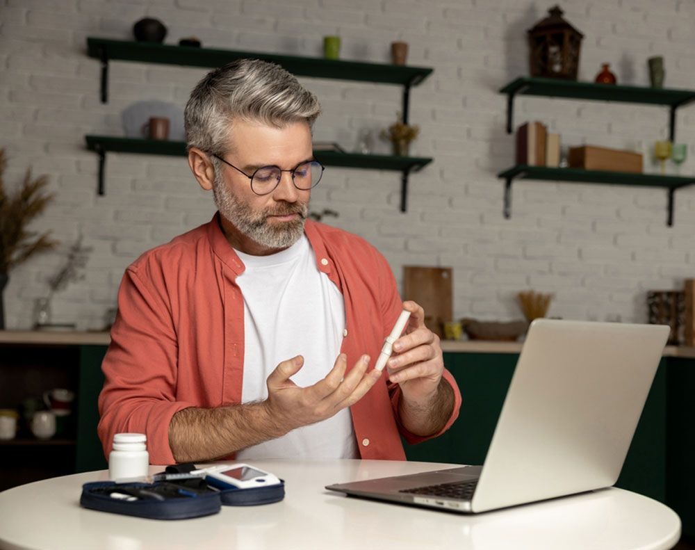 A man is sitting at a table with a laptop and a bottle of pills.