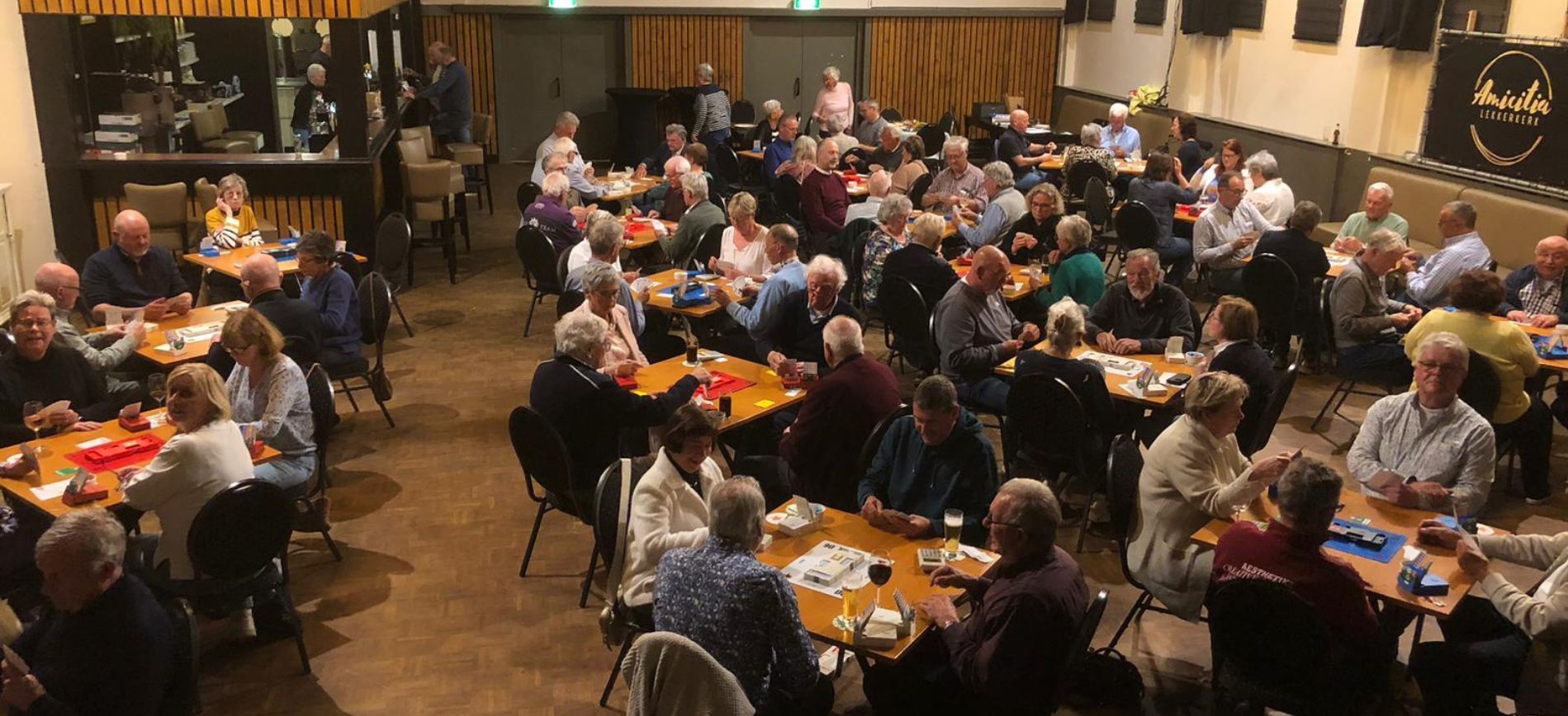 Spelers aan tafels tijdens een gezellige zomerbridgeavond in Amicitia in Lekkerkerk, georganiseerd d