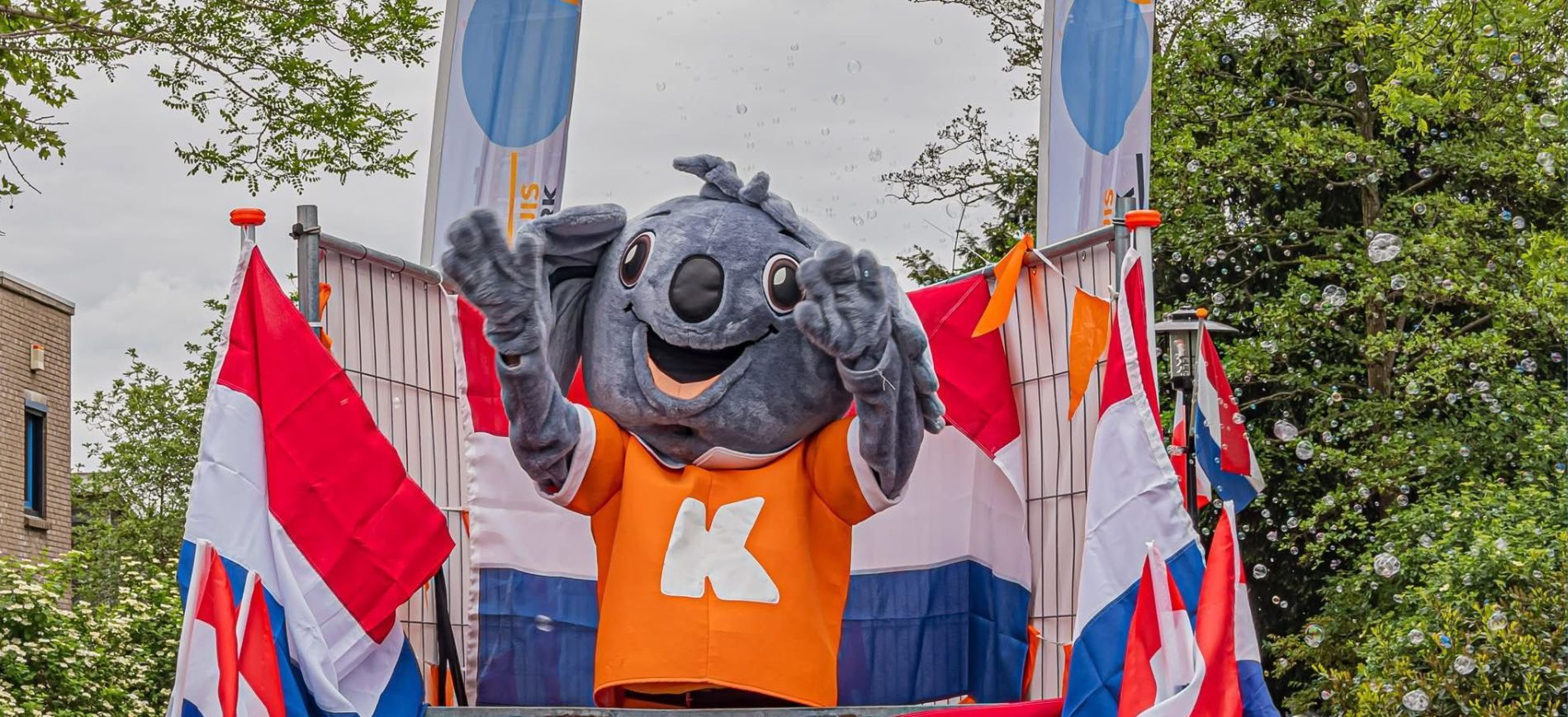 Mascotte in vrolijk kostuum begroet bezoekers tijdens de allegorische optocht, omringd door lachende