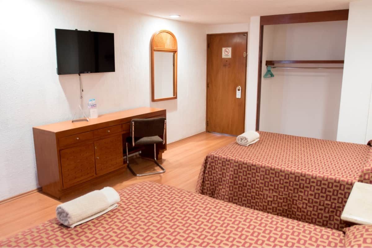 Una habitación de hotel con dos camas, un escritorio, una televisión y un espejo.